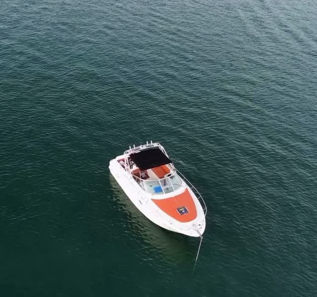 The Sea Ray Amberjack 32 anchored by itself in deep green water, coral bow cushions and the bimini up