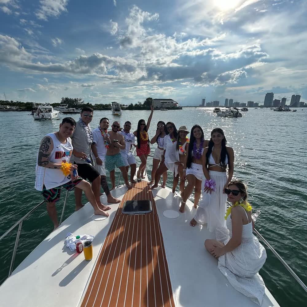 Guests standing along the Chris Craft's teak bow, drinks in hand, with the Miami skyline behind them