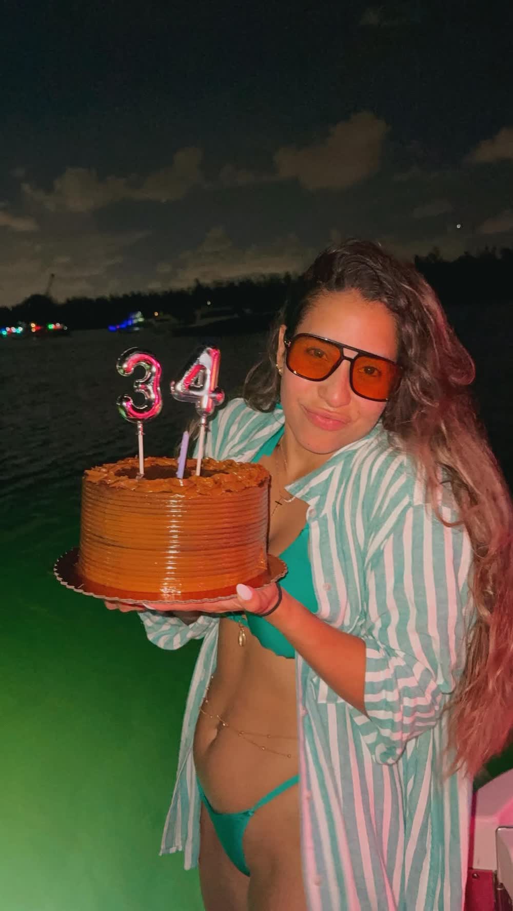 A guest holding a birthday cake with number candles, lit, on deck after dark