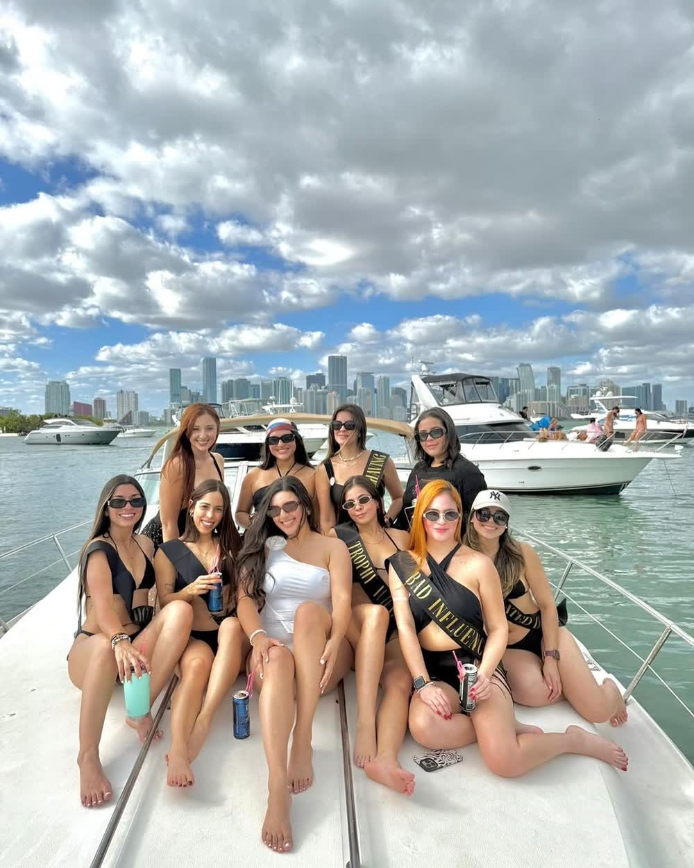 A bachelorette group spread along the bow of the Chris Craft with the Miami skyline behind them