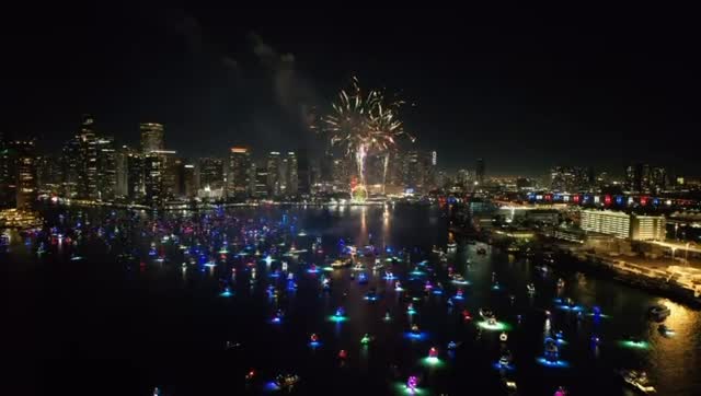 Boats gathered on the bay at night with the city lit up behind them