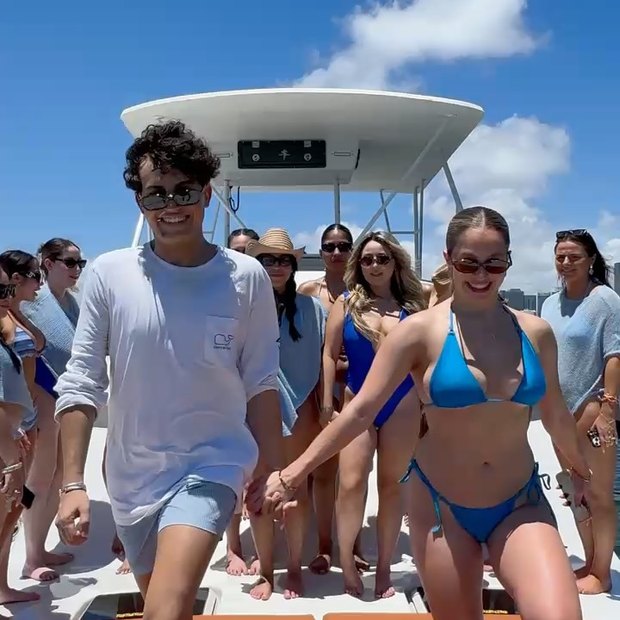 Un grupo en traje de baño en la proa bajo el hardtop, con una pareja caminando de la mano adelante