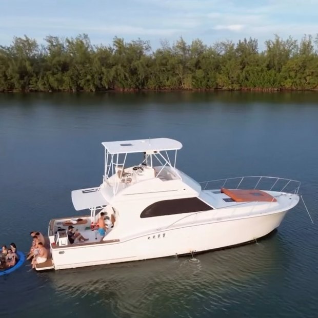 El Chris Craft fondeado junto a una costa de manglares, con invitados en la proa y un flotador en el agua