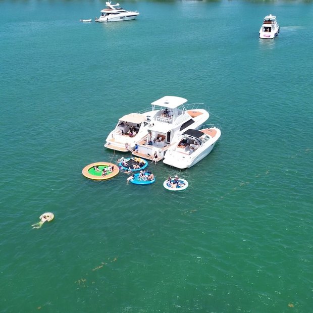 Dos botes de LuxSea amarrados juntos en agua turquesa con piscinas flotantes al lado, vistos desde arriba
