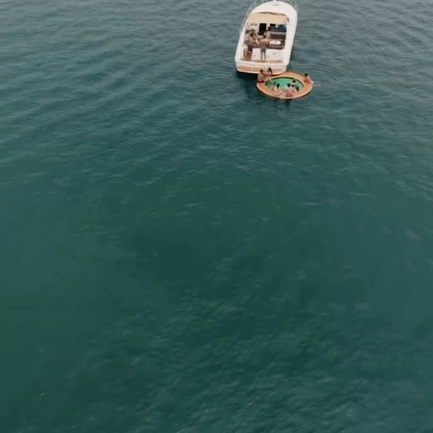 Un bote solo en agua verde y calma, visto desde muy arriba, con un flotador amarrado al costado
