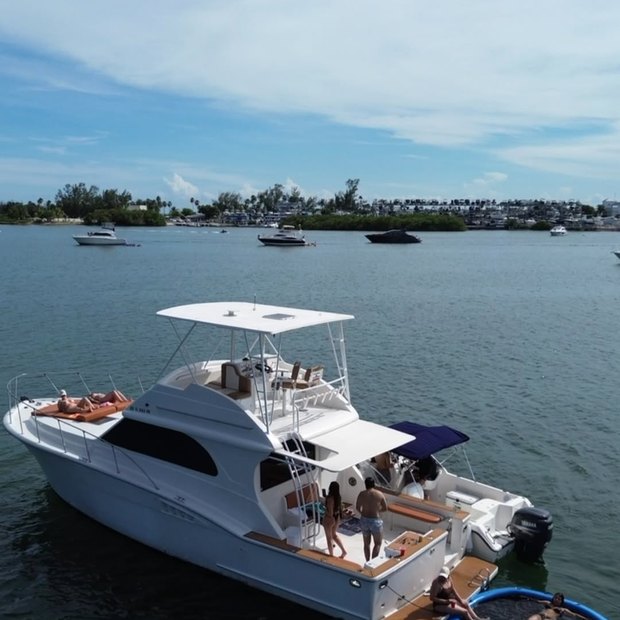 El Chris Craft fondeado frente a una costa arbolada, con invitados en la plataforma de baño
