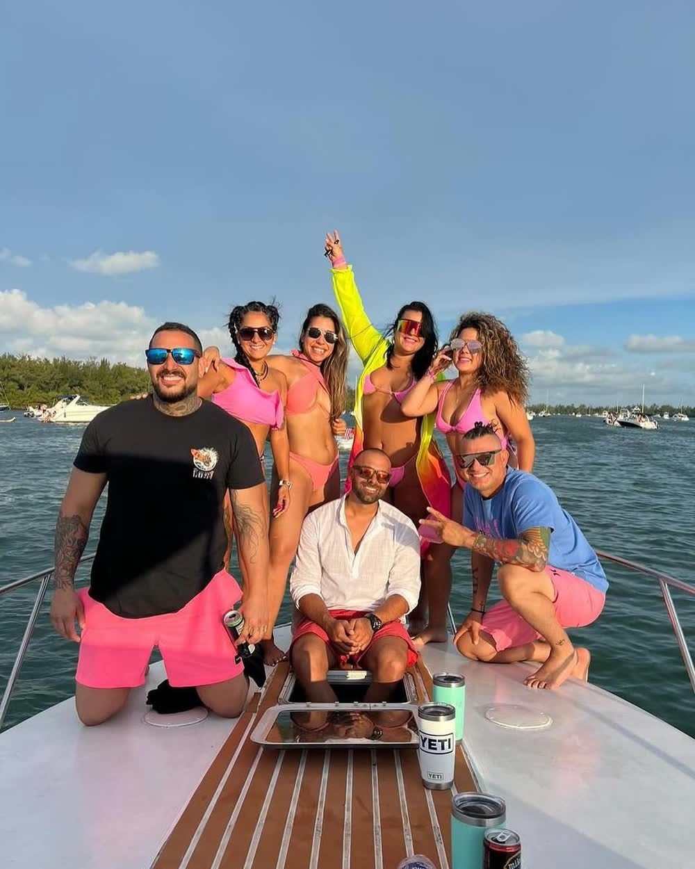 A group gathered on the teak bow around a tray of drinks, mangroves and other boats behind