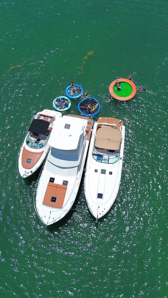 Overhead view of the three boats tied bow to stern in a line, floating pools trailing behind them in green water