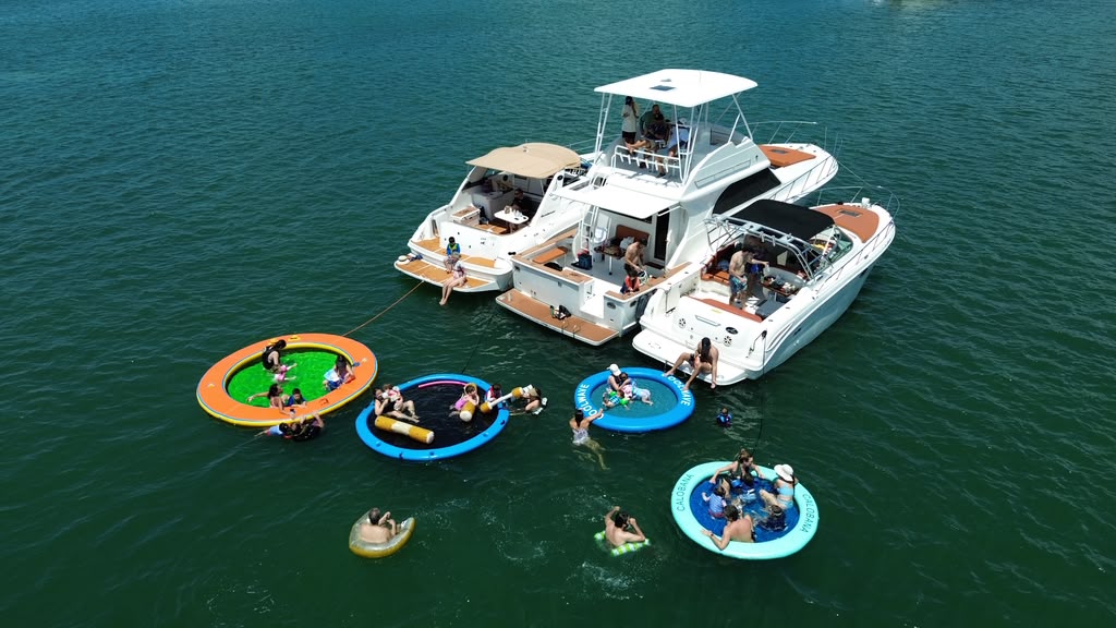 The three boats rafted together seen from the side, with four floating pools tied off and people sitting in them
